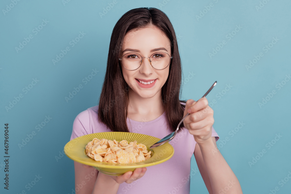 Photo of young woman happy positive smile morning food cereal granola healthy eyewear isolated over teal color background Photo of young woman happy positive smile morning food cereal granola healthy eyewear isolated over teal color background