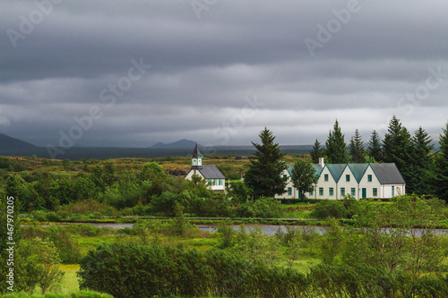 White houses and church with forest and green meadow on a cloudy day