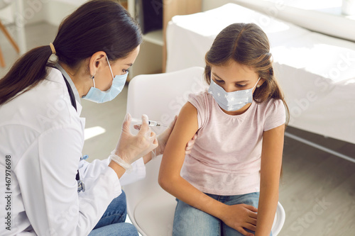 Vaccination. Portrait of little girl getting vaccinated against viral disease or coronavirus infection. Female doctor or nurse in medical mask and gloves gives child injection in arm at medical clinic