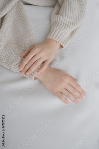Woman hands. Woman closeup picture without face on neutral background. White interior. Very soft and nice light. Healthy and clean skin. Comfort and calm. French manicure. Good nails. Beige sweater