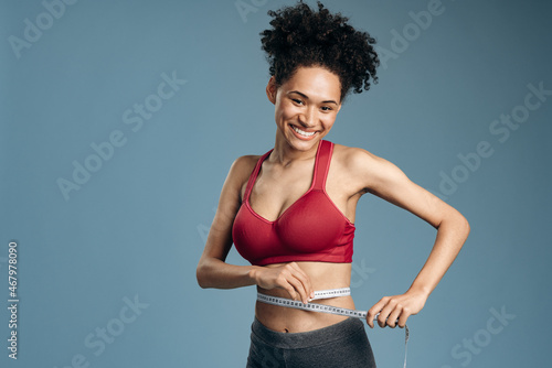 Smiling multiracial woman with beautiful body measuring her waist with measurement type after diet