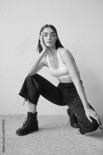 Beautiful slim woman in studio. Black and white photo. European model. Fashionable look, nude makeup. Teenager. With amazing eyes, light skin and dark hair. Long legs. Soft light. Emotional portrait
