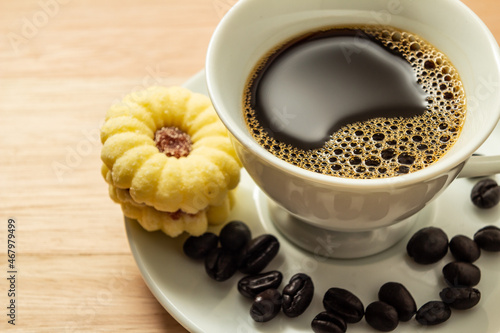 Uma xícara de café com grãos espalhados e um biscoito amanteigado. photo