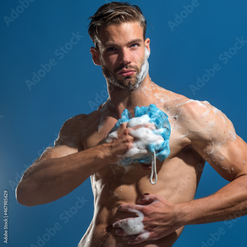 Muscular bearded hipster washes in shower. Handsome muscular sexy attractive bearded man washing body with soap sponge. Sexy naked macho taking shower with soap sponge. Man washing his torso. Skincare