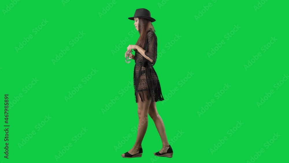 Side view of walking young woman in beachwear drinking water from bottle. Full body isolated on green screen background Side view of walking young woman in beachwear drinking water from bottle. Full body isolated on green screen background