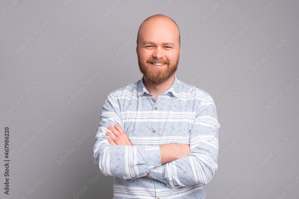 Portrait of young cheerful bearded man with crossed arms standing over grey background and smiling Portrait of young cheerful bearded man with crossed arms standing over grey background and smiling