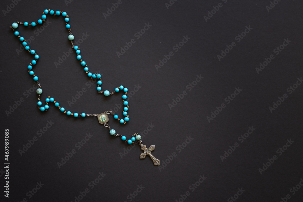 Rosary with blue beads on a black background with copy space