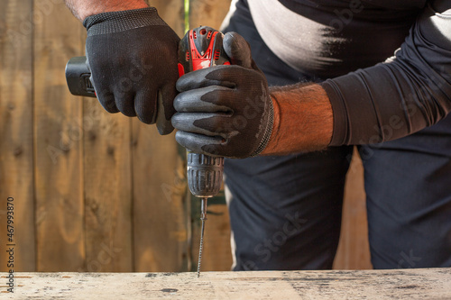 A man holds a cordless screwdriver in his hand and wraps the screw in a Board.