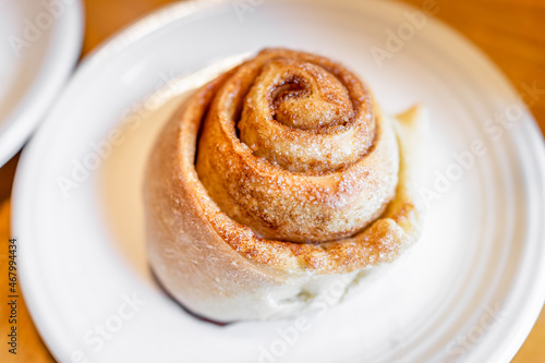 Large cooked baked cinnamon bun roll swirl dessert on white plate with sugar crust on kitchen table
