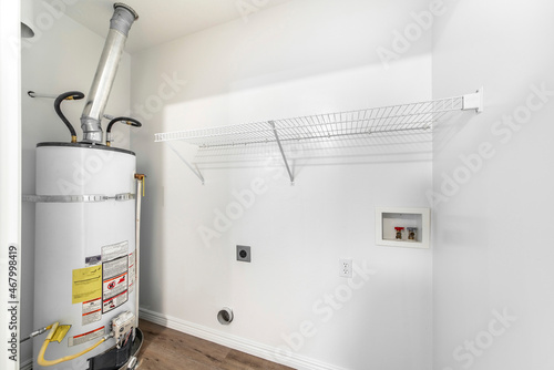 Empty white laundry room with water heater tank and wall mounted wire shelf