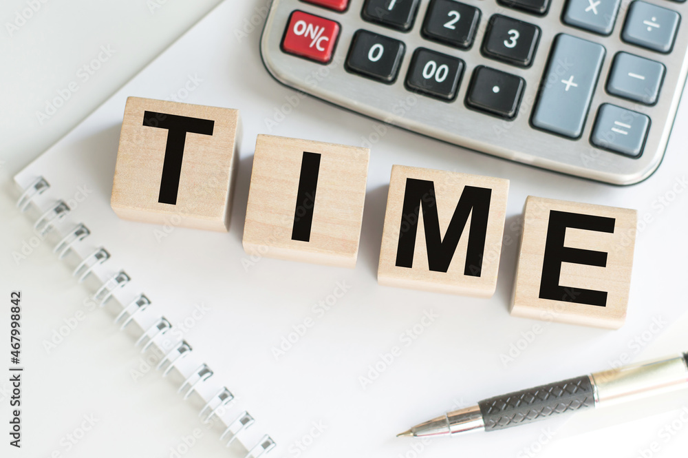 Text Time on wooden cubes on a notebook next to a pen and a calculator on the table. Text Time on wooden cubes on a notebook next to a pen and a calculator on the table.
