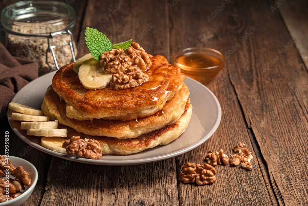 A stack of homemade pancakes with honey and nuts and a banana on a wooden background.