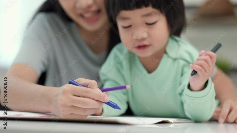 Happy asian boy painting with crayon and colored pencil with his mother in living room at home. Mom teaching son how to painting with crayon color on book or doing homework. family concept. Happy asian boy painting with crayon and colored pencil with his mother in living room at home. Mom teaching son how to painting with crayon color on book or doing homework. family concept.