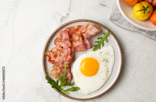 English breakfast. Egg and fried bacon. A cup with tomatoes. Serving breakfast on a marble table. Fried egg.