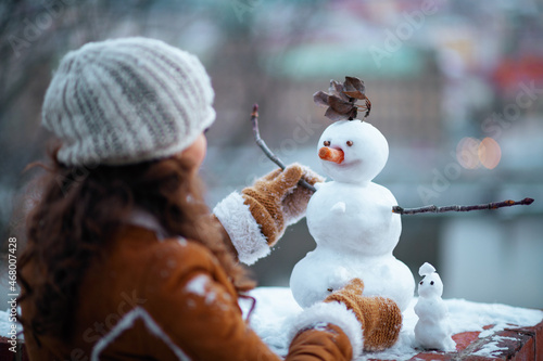 stylish woman making snowman outside in city park in winter