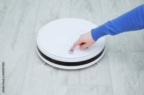 Caucasian woman presses her finger on  button on the cleaning robot vacuum cleaner. photo