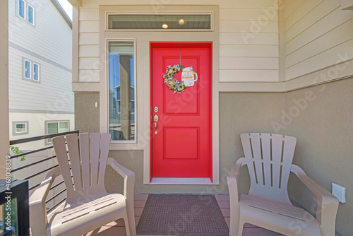 Entrance exterior of a house with two armchairs and red front door with wreath