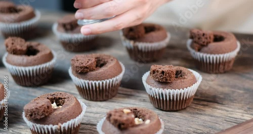 Chocolate muffins on wooden table. Hands of confectioner sprinkle pastries with nuts on cupcakes.