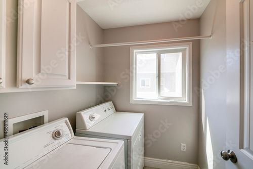 Laundry room interior with light gray wall and white cabinets and laundry units