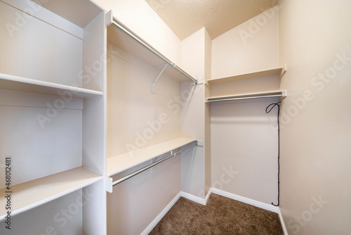 Narrow windowless walk-in closet with shelves and metal rods