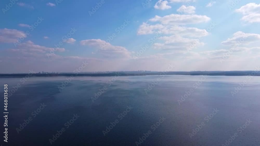 Smooth aerial flight up over a blue lake and a city on the horizon Smooth aerial flight up over a blue lake and a city on the horizon