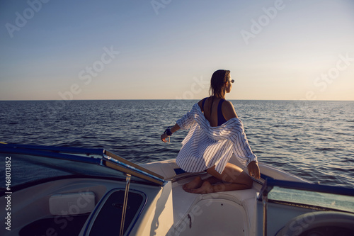 young sexy woman in a blue swimsuit and shorts is sitting on bow of a yacht in the summer on vacation