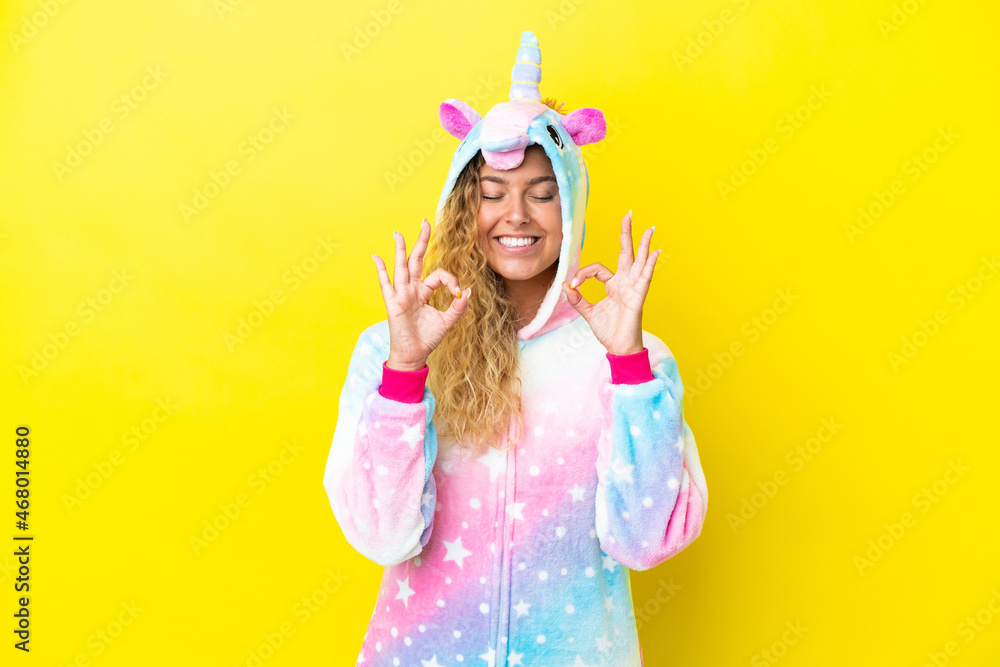 Girl with curly hair wearing a unicorn pajama isolated on yellow background in zen pose Girl with curly hair wearing a unicorn pajama isolated on yellow background in zen pose