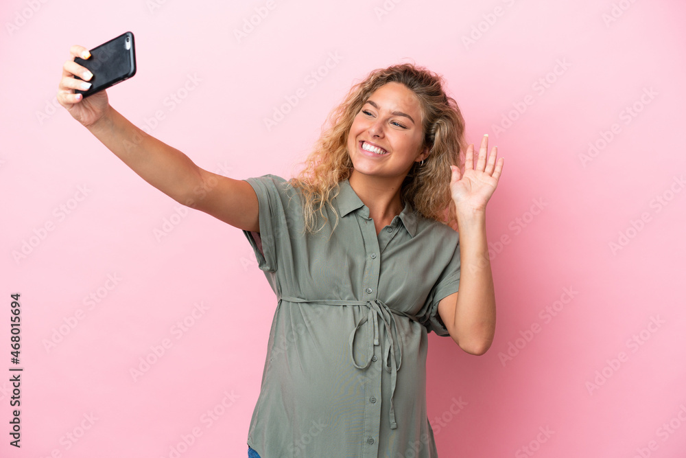 Girl with curly hair isolated on pink background pregnant and making a selfie Girl with curly hair isolated on pink background pregnant and making a selfie