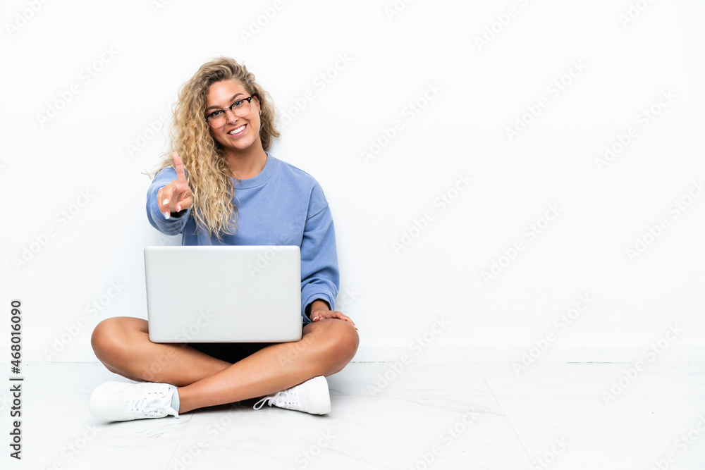 Fototapeta premium Girl with curly hair with a laptop sitting on the floor showing and lifting a finger