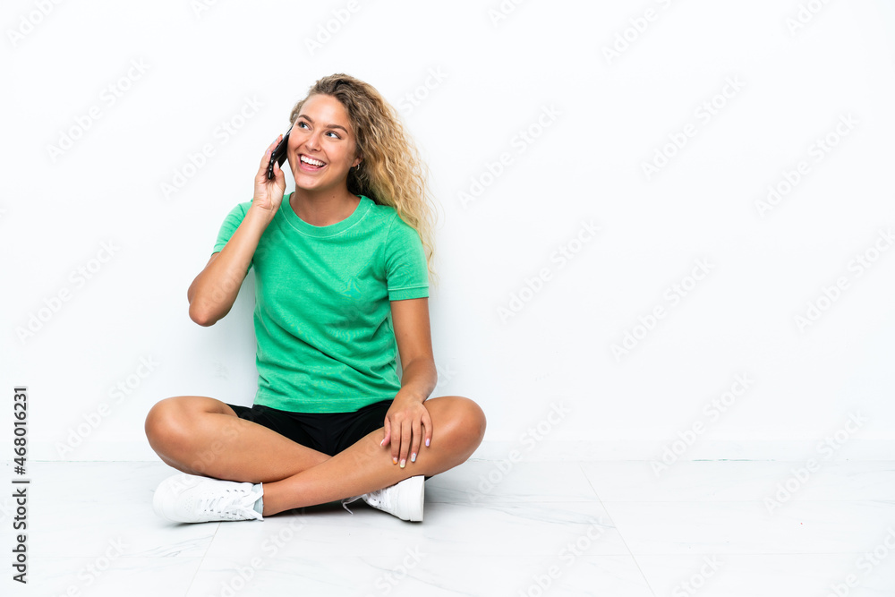 Girl with curly hair sitting on the floor keeping a conversation with the mobile phone Girl with curly hair sitting on the floor keeping a conversation with the mobile phone