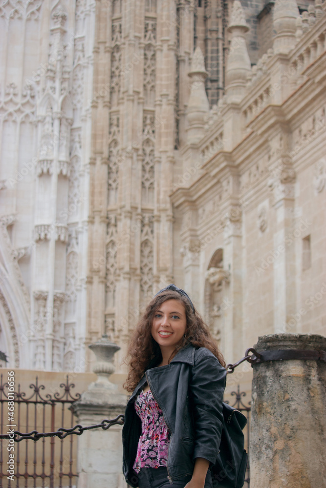 Caucasian tourist girl poses smiling towards the camera with Seville cathedral in the background.