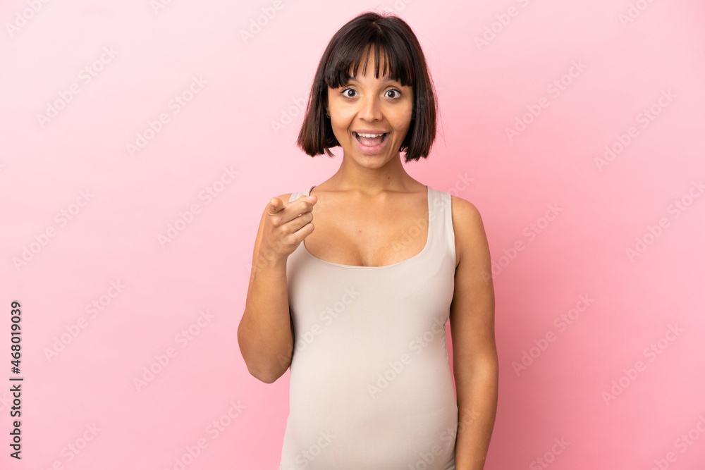 Young pregnant woman over isolated pink background surprised and pointing front Young pregnant woman over isolated pink background surprised and pointing front