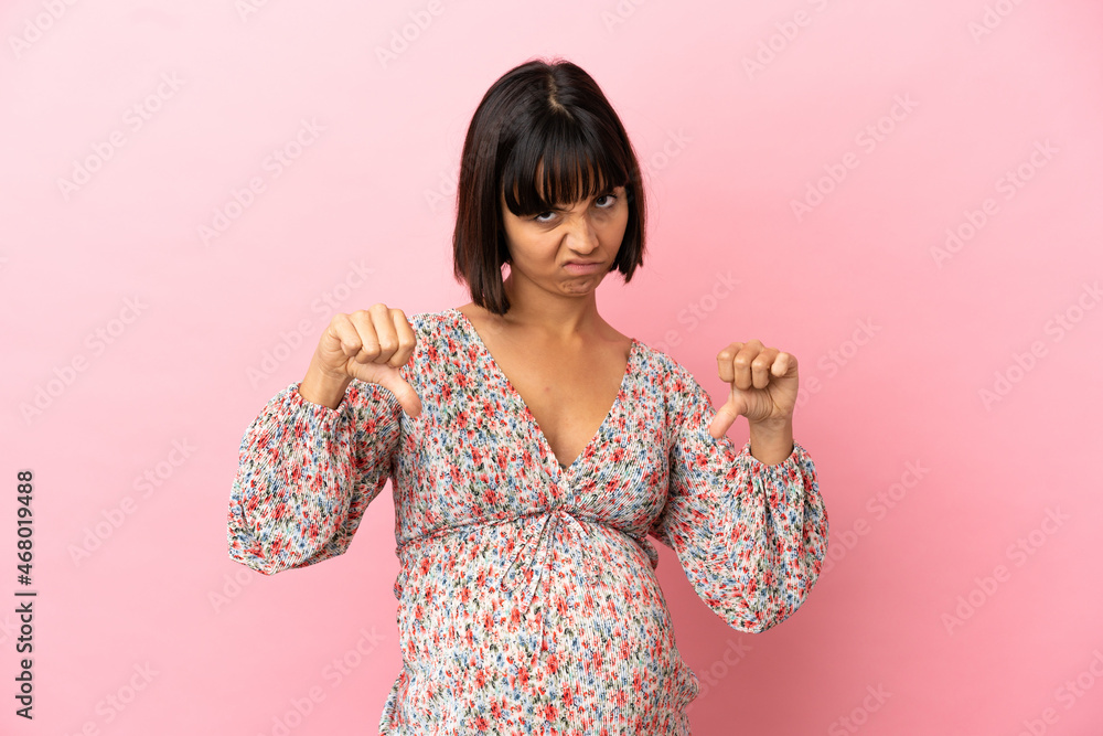 Young pregnant woman over isolated pink background showing thumb down with two hands Young pregnant woman over isolated pink background showing thumb down with two hands