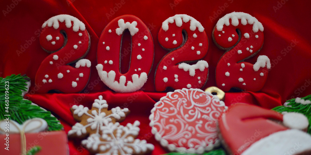 Banner for Christmas and New Year gingerbread cookies numbers 2022, snowflakes, Santa hat, Christmas trees, garlands on red silk fabric background