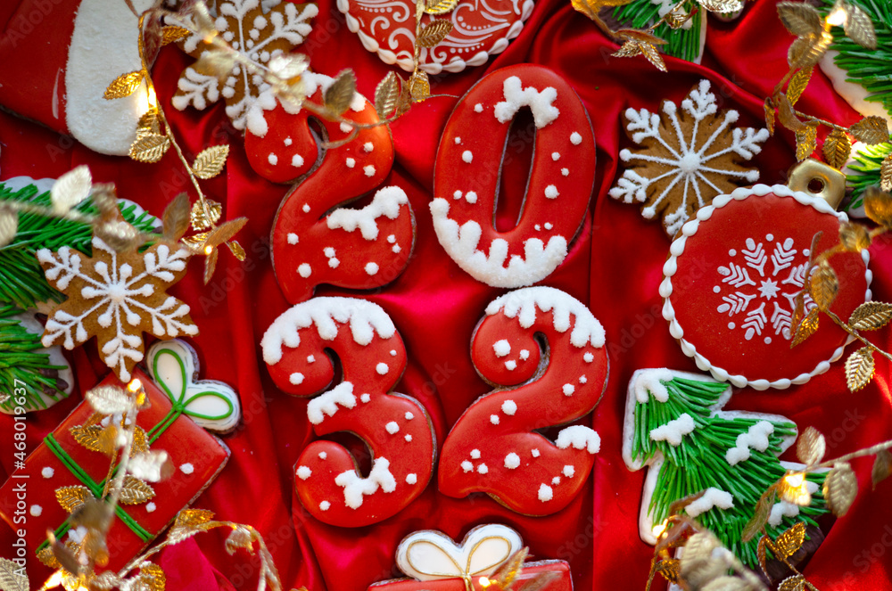 Banner for Christmas and New Year gingerbread cookies numbers 2032, snowflakes, Santa hat, Christmas trees, garlands on red silk fabric background Banner for Christmas and New Year gingerbread cookies numbers 2032, snowflakes, Santa hat, Christmas trees, garlands on red silk fabric background