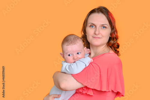 Mom with an infant child on a yellow studio background. A woman holds a baby four months old in her arms