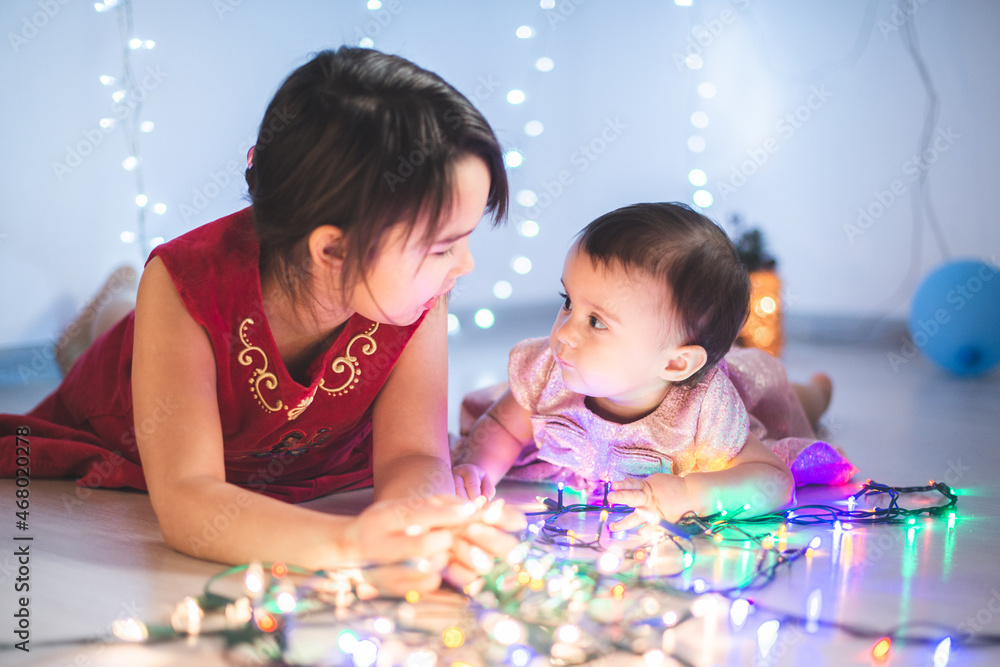 Fototapeta premium Little sisters having fun at home with chrismass lights.