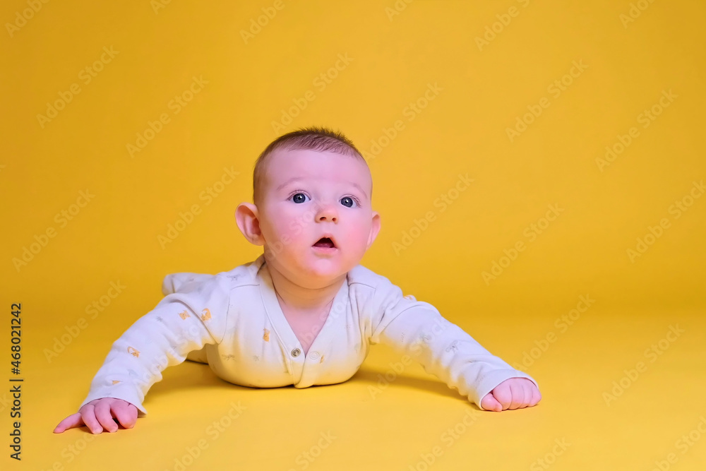 Infant baby boy looks in surprise while lying on his tummy, studio yellow background. Four month old child close up Infant baby boy looks in surprise while lying on his tummy, studio yellow background. Four month old child close up