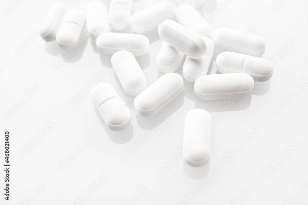 White medicine pills spilled on white background. Selective focus. White medicine pills spilled on white background. Selective focus.