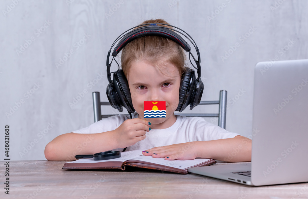 School female child with Kiribati flag. Child in headphones, with a book and laptop has lesson online School female child with Kiribati flag. Child in headphones, with a book and laptop has lesson online