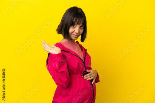 Young pregnant woman over isolated yellow background holding copyspace imaginary on the palm to insert an ad © luismolinero