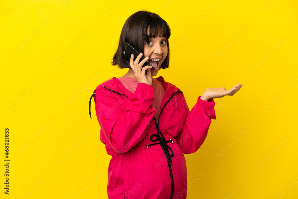 Young pregnant woman over isolated yellow background keeping a conversation with the mobile phone with someone Young pregnant woman over isolated yellow background keeping a conversation with the mobile phone with someone