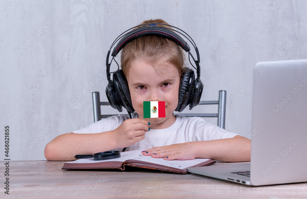 School female child with Mexico flag. Child in headphones, with a book and laptop has lesson online School female child with Mexico flag. Child in headphones, with a book and laptop has lesson online
