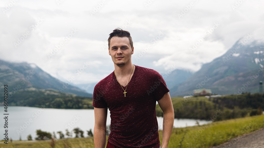 man posing on a mountaintop with hotel and lake in the background man posing on a mountaintop with hotel and lake in the background