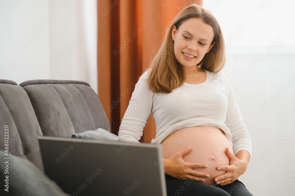 Pregnant woman video chatting with family on laptop waving hand to screen Pregnant woman video chatting with family on laptop waving hand to screen