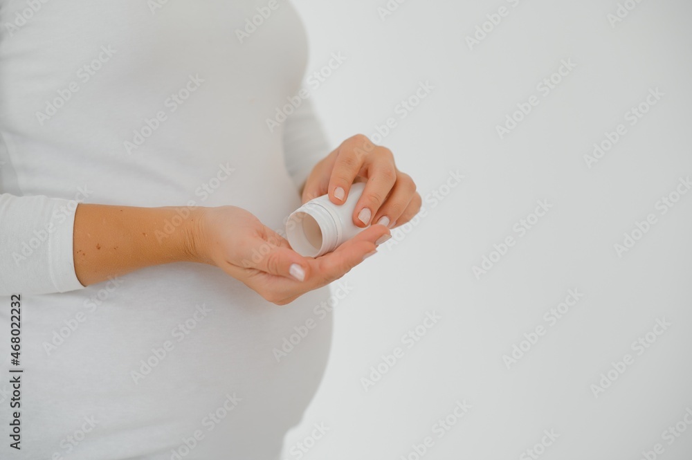 Close up on pregnant belly with medicine..Woman expecting a baby dressed in white holding pills. Taking drugs or vitamins during pregnancy concept. Close up on pregnant belly with medicine..Woman expecting a baby dressed in white holding pills. Taking drugs or vitamins during pregnancy concept.