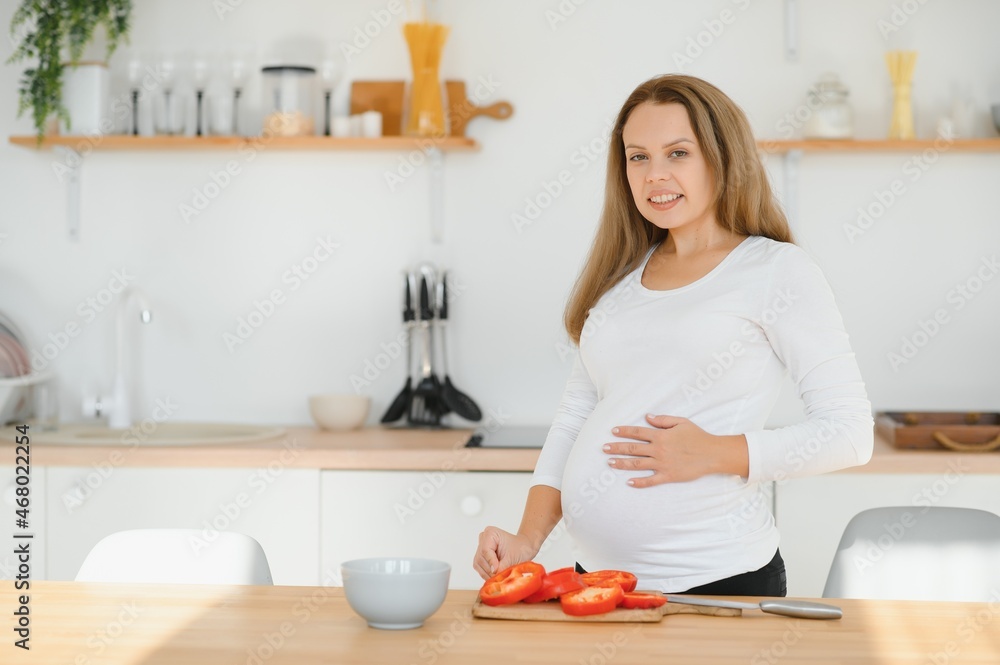 pregnancy, cooking food, healthy lifestyle, people and expectation concept - happy pregnant woman with knife chopping cucumber and preparing vegetable salad at home pregnancy, cooking food, healthy lifestyle, people and expectation concept - happy pregnant woman with knife chopping cucumber and preparing vegetable salad at home