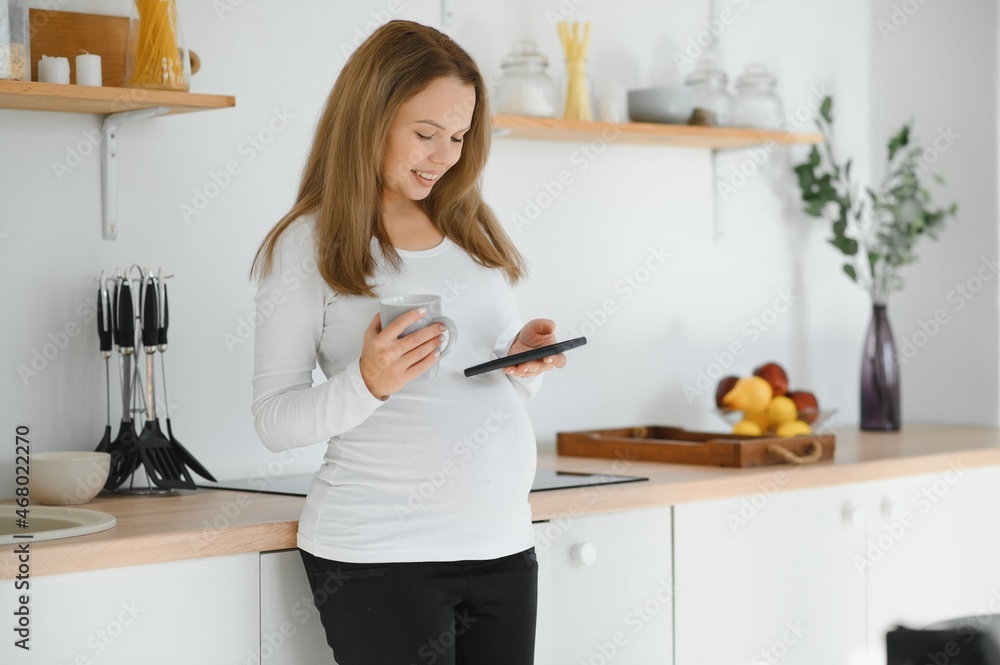 So nice to hear you Beautiful young pregnant woman talking on phone and looking away with smile while standing at kitchen interior So nice to hear you Beautiful young pregnant woman talking on phone and looking away with smile while standing at kitchen interior