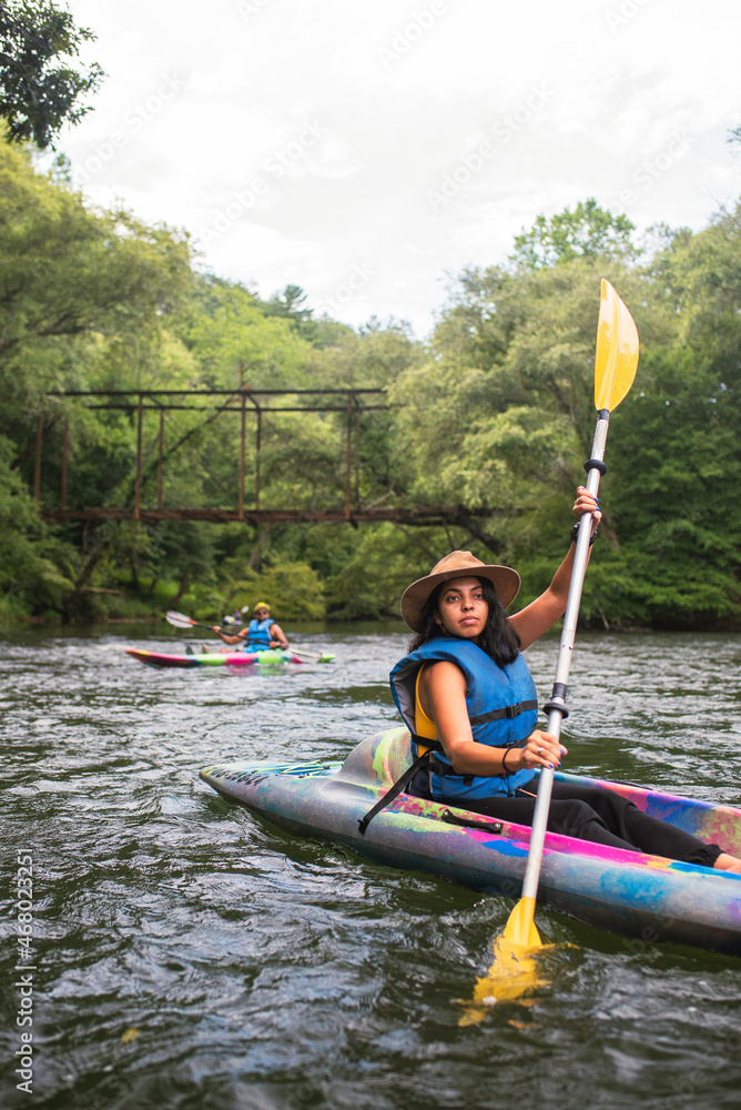 Woman and man kayaking on river with trees and footbridge in background Woman and man kayaking on river with trees and footbridge in background