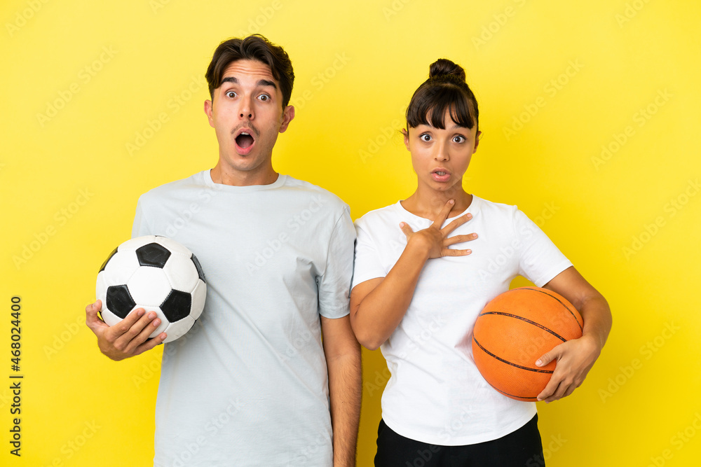 young sport couple playing football and basketball isolated on yellow background with surprise and shocked facial expression